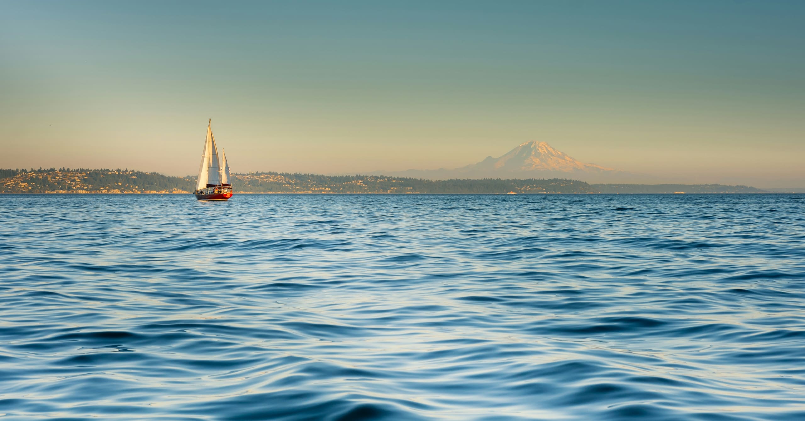 A sailboat on Puget Sound in evening light, with Mount Rainier behind it.